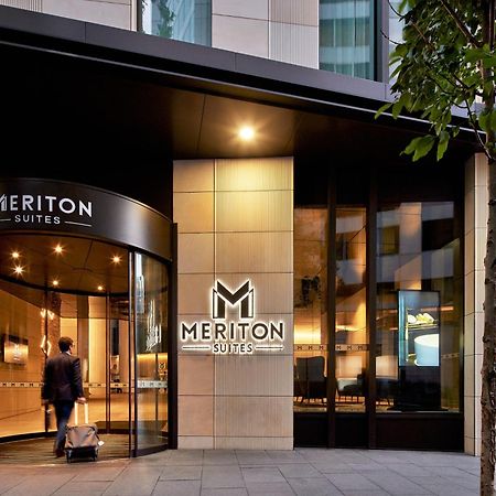 Meriton Suites Sussex Street, Sydney Exteriér fotografie The photo shows the entrance of a hotel or suite establishment named "Meriton Suites." The entrance features a revolving door and a large, illuminated sign with the name "MERITON SUITES." The facade is modern and sleek, with a combination of glass an