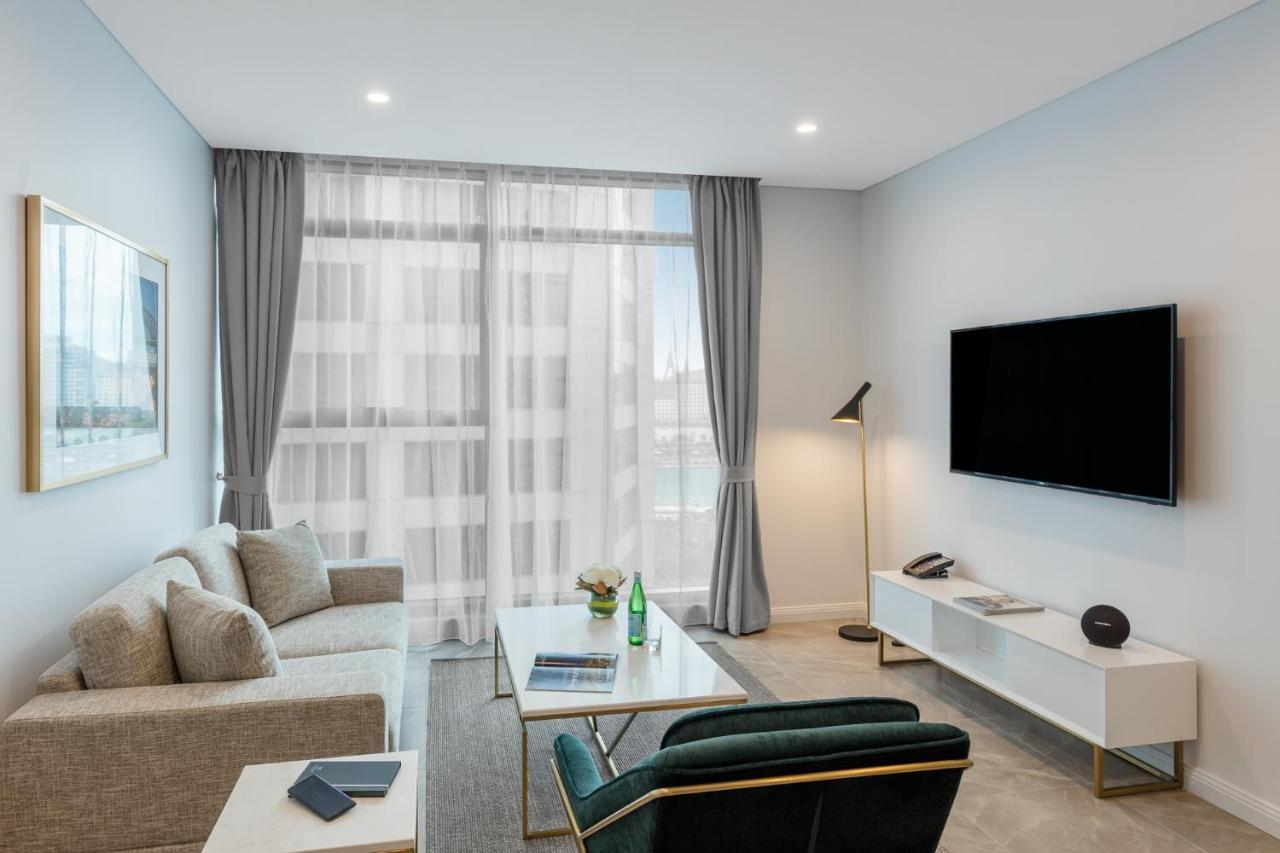 Meriton Suites Sussex Street, Sydney Exteriér fotografie The photo shows a modern living room space with a light, airy ambiance. It features a comfortable beige sofa with decorative cushions, a sleek coffee table placed in front, and a dark green armchair. There is a large window covered with sheer curtain