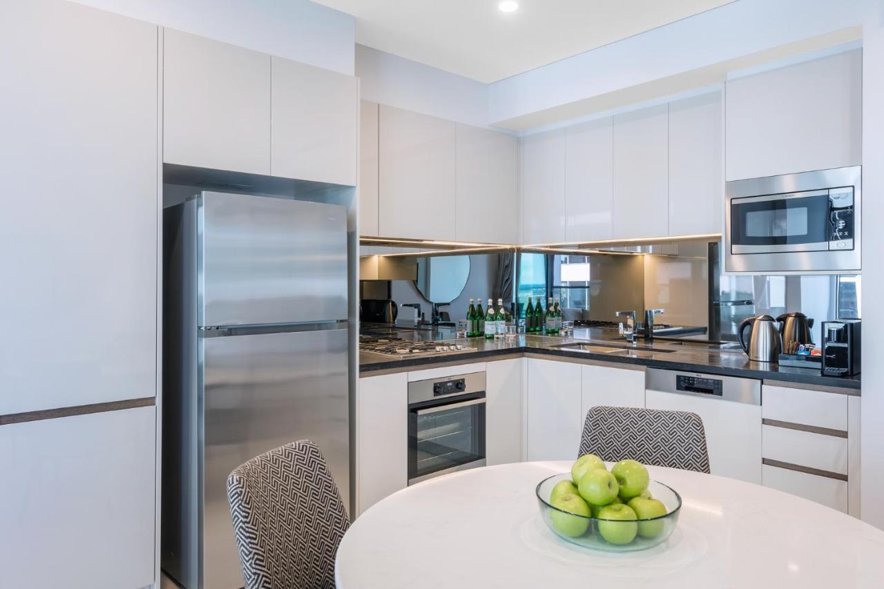 Meriton Suites Sussex Street, Sydney Exteriér fotografie The photo displays a modern kitchen with a sleek design. It features light-colored cabinetry and a countertop with a polished finish. On the left, there is a stainless steel refrigerator. The kitchen is equipped with various appliances, including an 