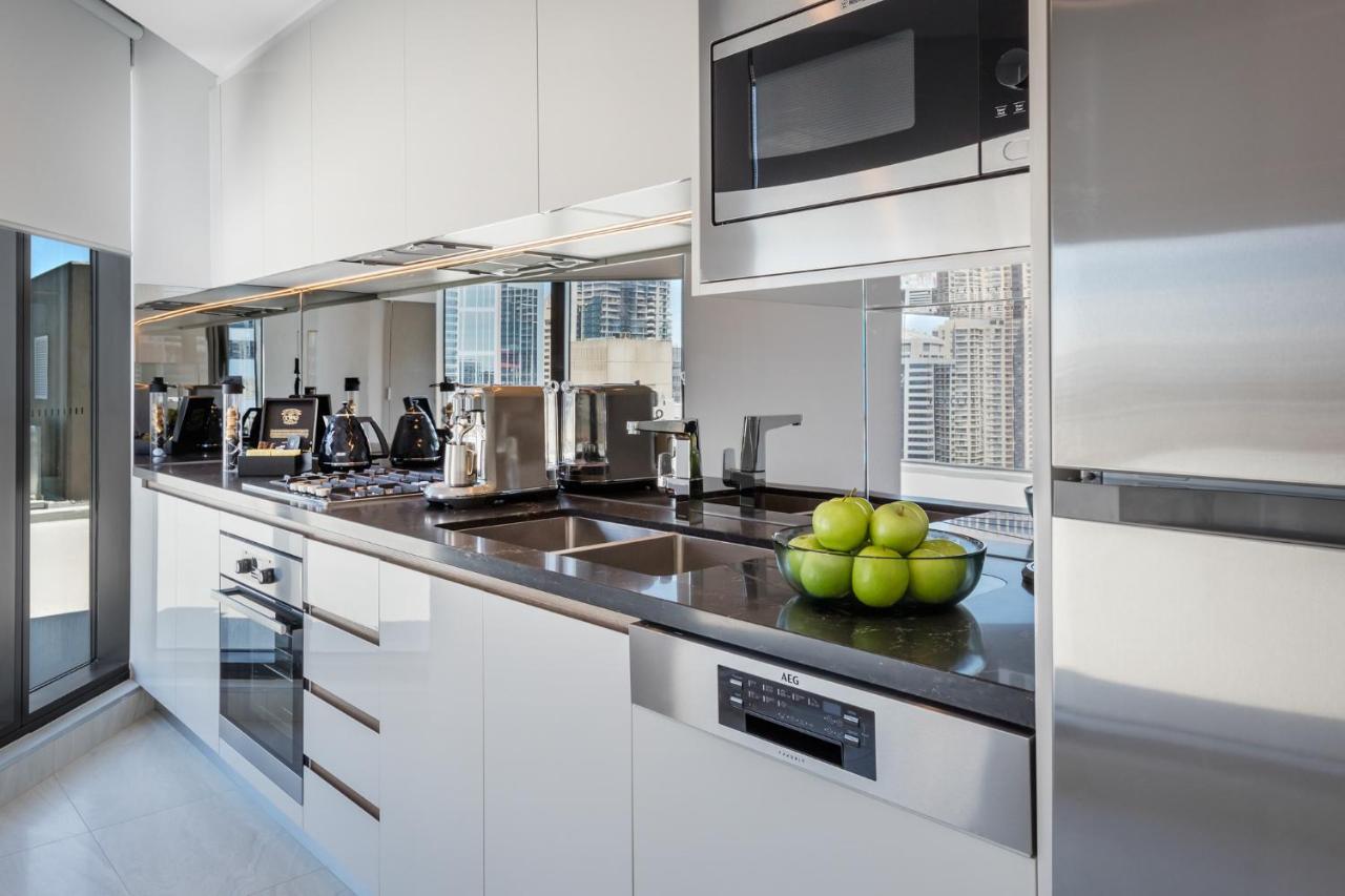 Meriton Suites Sussex Street, Sydney Exteriér fotografie The photo shows a modern kitchen featuring sleek cabinetry and stainless steel appliances. There is a glossy countertop with a bowl of green apples as a decoration. The kitchen includes a built-in oven, a microwave, and other kitchen gadgets, along w