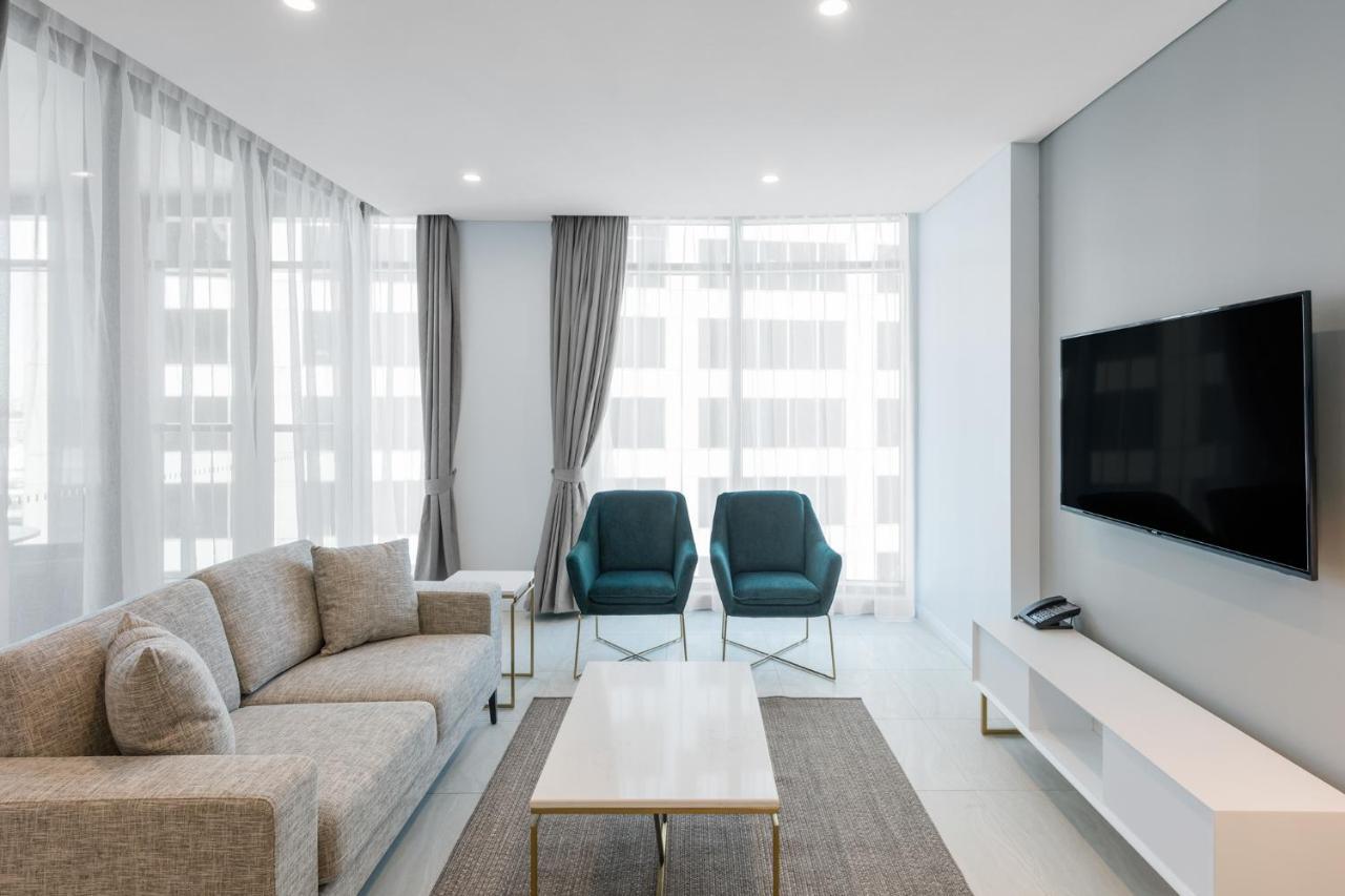 Meriton Suites Sussex Street, Sydney Exteriér fotografie The photo shows a modern living room equipped with a light gray sofa, two teal chairs, and a coffee table in the center. The room features large windows with sheer curtains, allowing natural light to illuminate the space. There is a white media conso