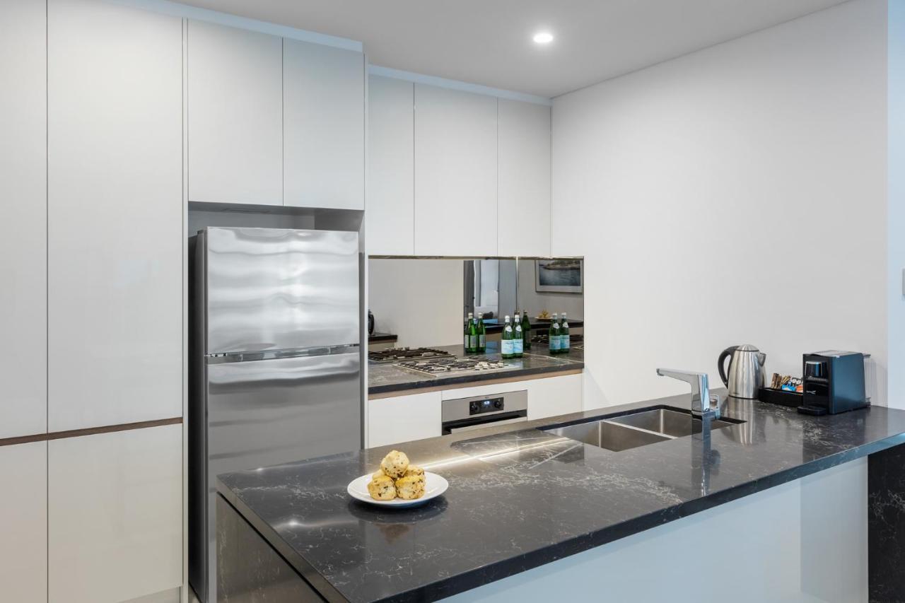 Meriton Suites Sussex Street, Sydney Exteriér fotografie The photo shows a modern kitchen with a sleek, minimalist design. Key features include:

- A shiny stainless steel refrigerator on the left.
- A mirrored backsplash above the stove, which has a gas burner.
- A dark countertop made of what appears to 