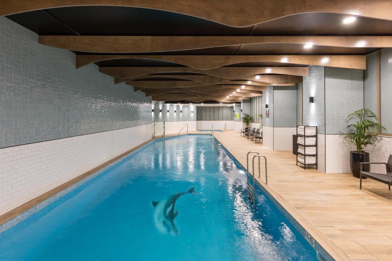 Meriton Suites Sussex Street, Sydney Exteriér fotografie The photo shows an indoor swimming pool. The pool features clear blue water, and there is a dolphin swimming in it. The surrounding area has a modern design with curved wooden beams on the ceiling, and the walls are tiled in light colors. There are a