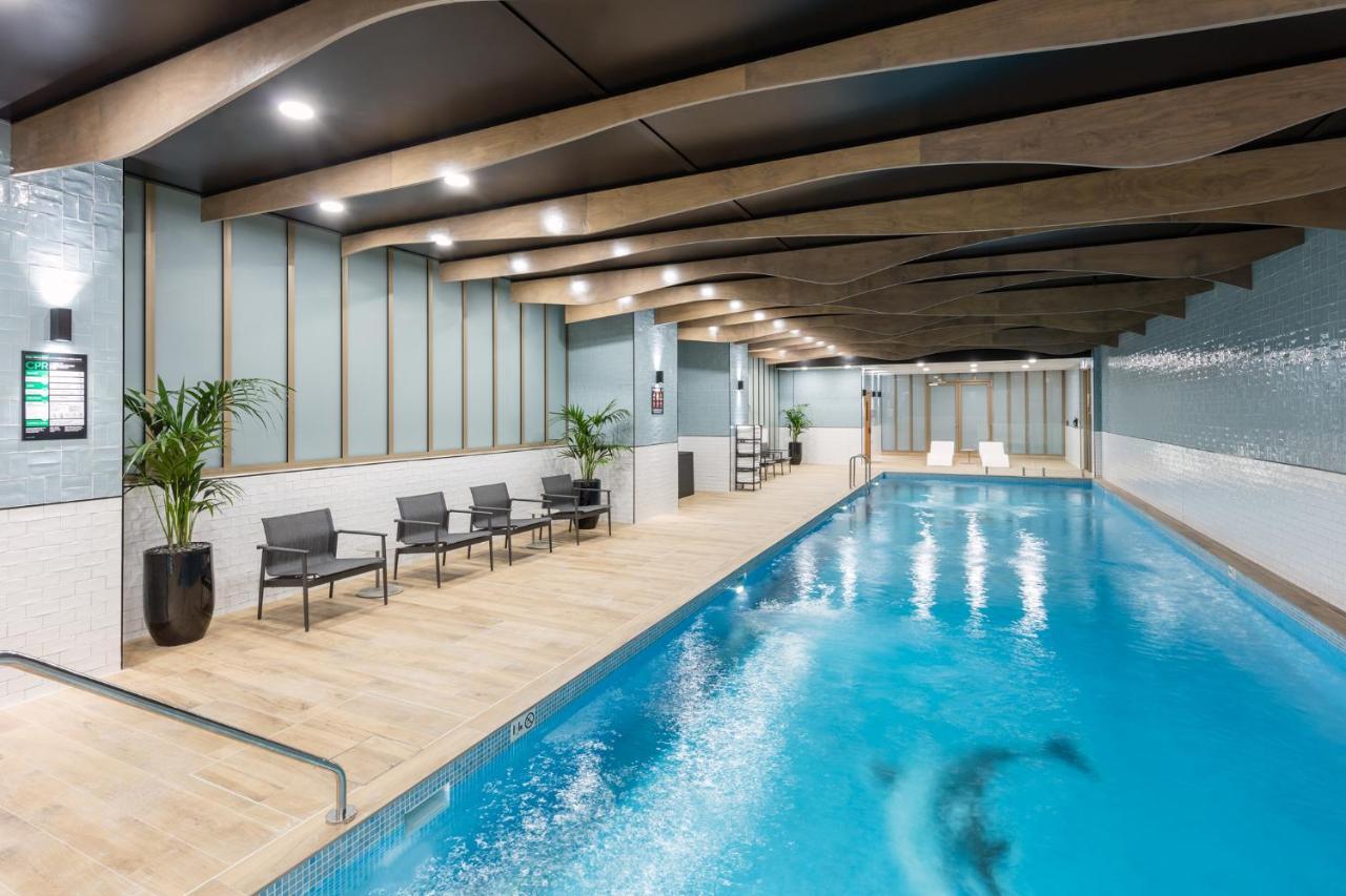 Meriton Suites Sussex Street, Sydney Exteriér fotografie The photo shows an indoor swimming pool area. The pool has clear blue water and is flanked by a wooden deck. There are several lounge chairs arranged along one side of the pool. The ceiling features a modern design with wooden beams and recessed ligh