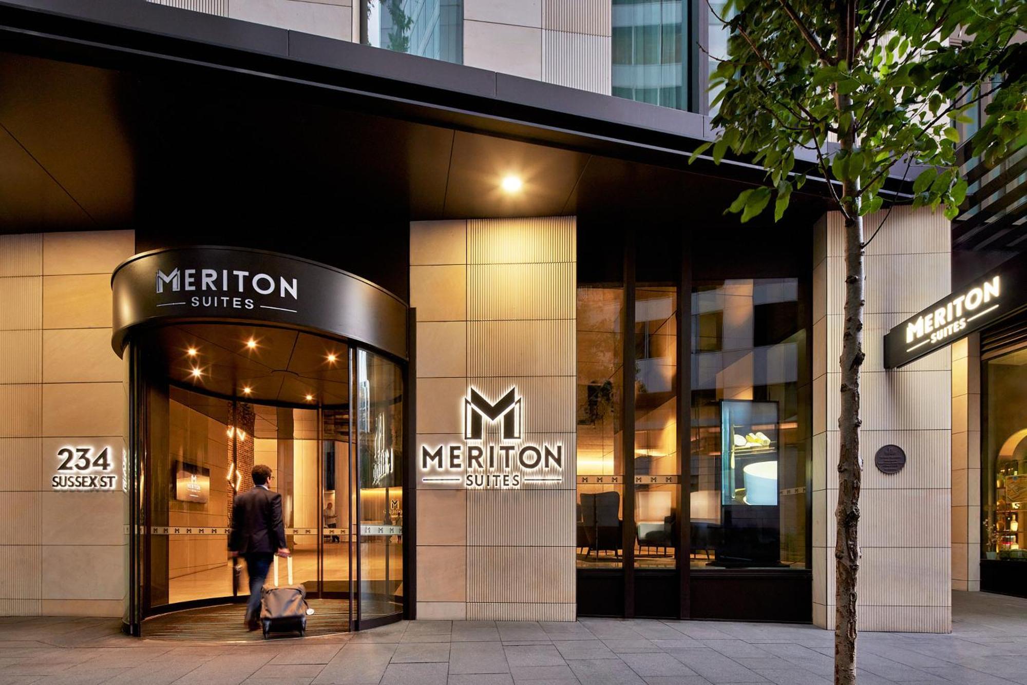 Meriton Suites Sussex Street, Sydney Exteriér fotografie The photo shows the entrance of a hotel or suite establishment named "Meriton Suites." The entrance features a revolving door and a large, illuminated sign with the name "MERITON SUITES." The facade is modern and sleek, with a combination of glass an