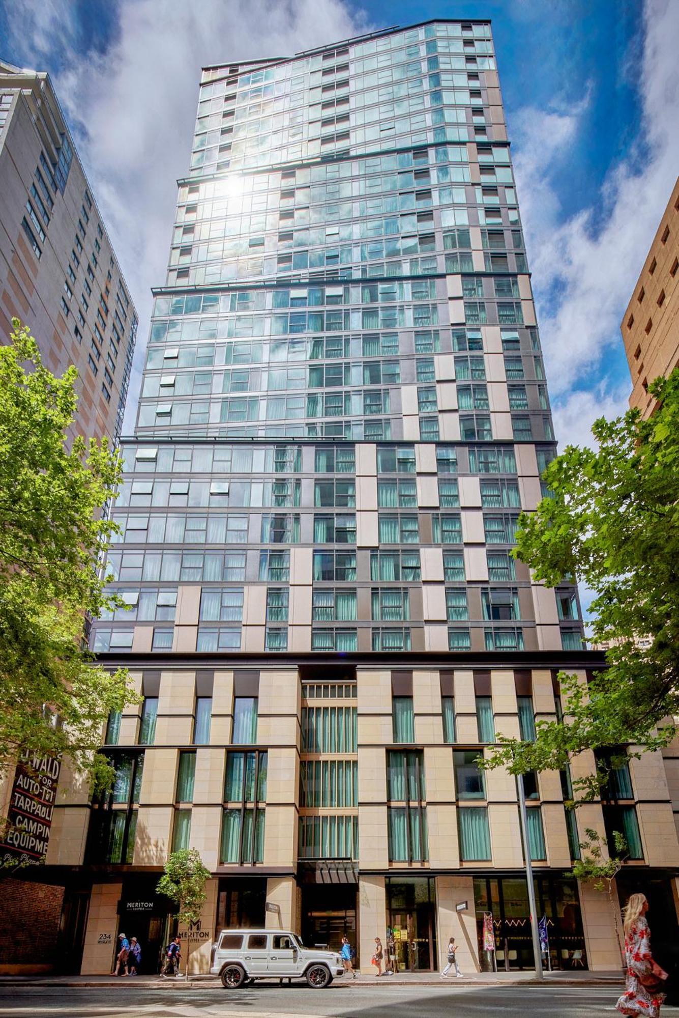 Meriton Suites Sussex Street, Sydney Exteriér fotografie The photo shows a tall modern building with a glass facade and various architectural design elements. The structure has multiple stories, with large windows that reflect the surrounding environment. At the base, there are sections that appear to have