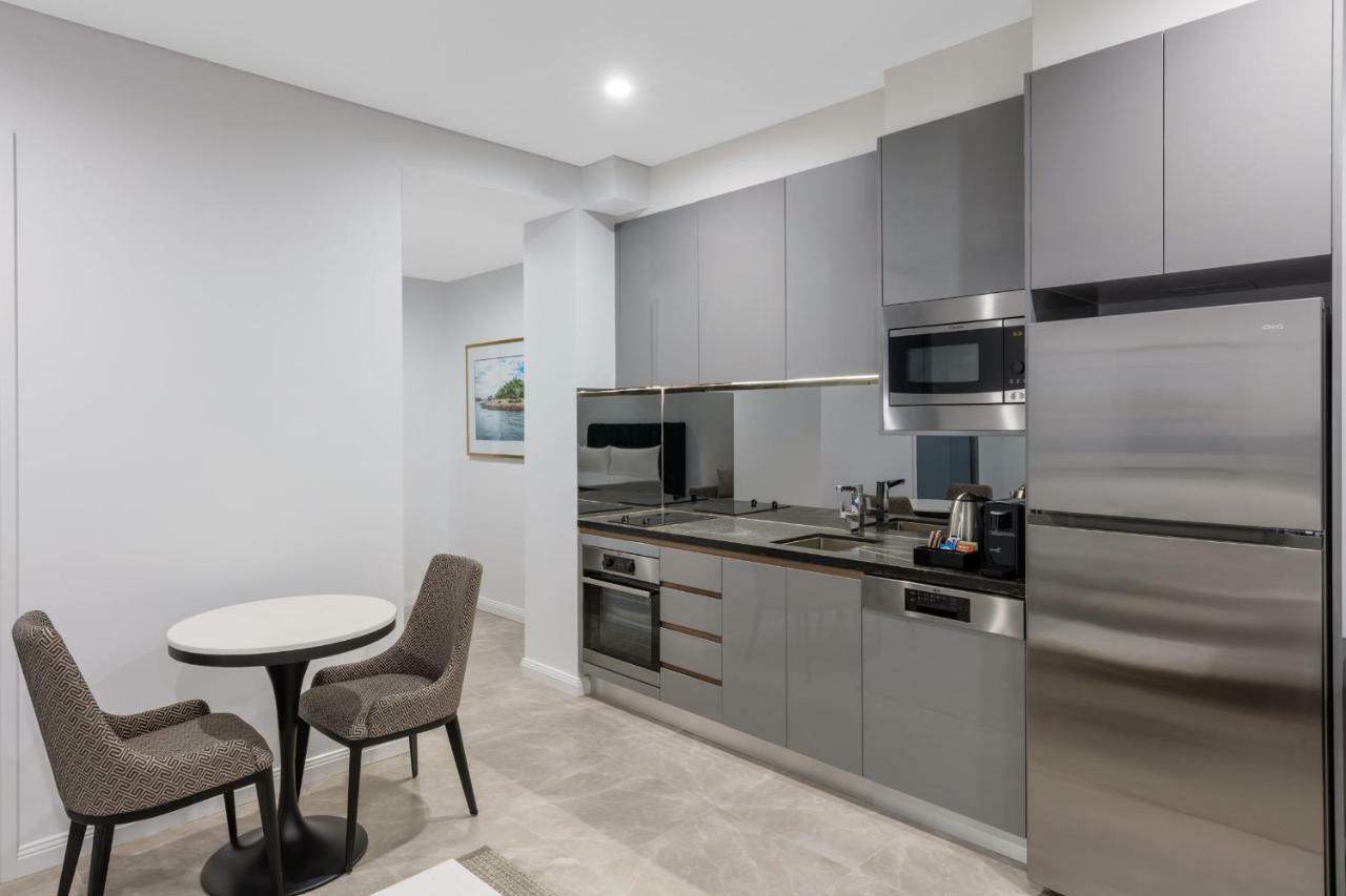 Meriton Suites Sussex Street, Sydney Exteriér fotografie The photo shows a modern kitchen area that features a sleek design. The cabinetry and appliances are in shades of gray, giving it a contemporary look. There is a stainless steel refrigerator, microwave, and oven, along with a sink and cooking area. 
